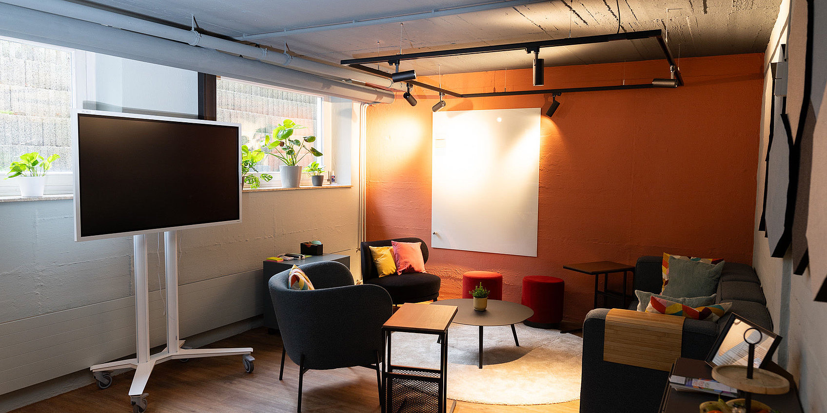 Gemütliche Meetinglounge mit digitalem Flipchart, Whiteboard, Sesseln und Sofa