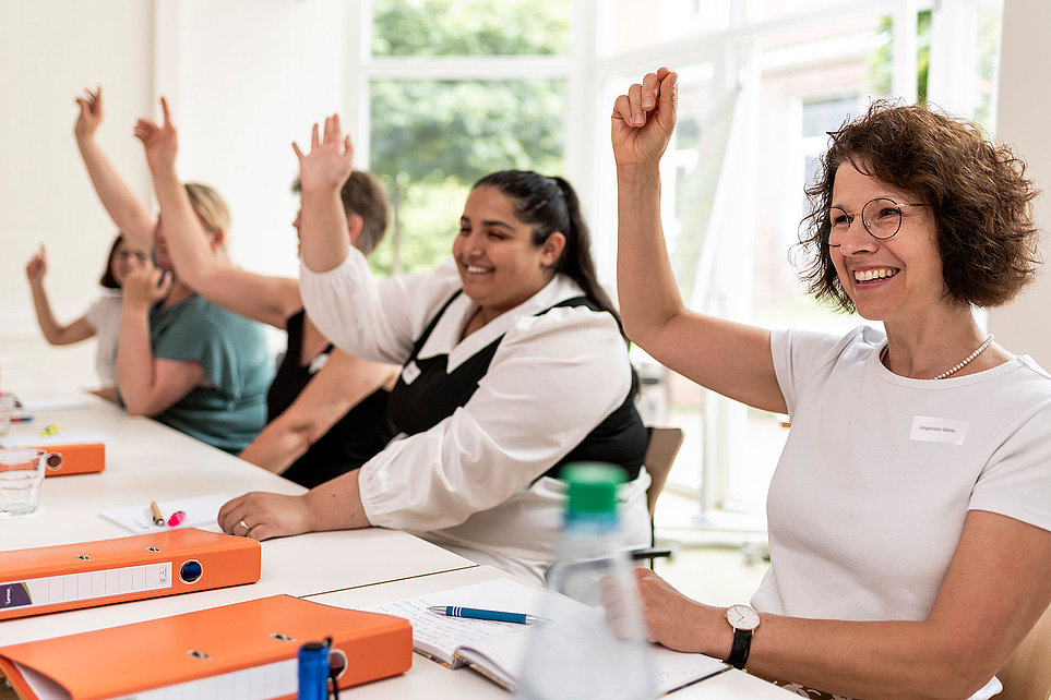 Mitarbeitende bei Besprechung heben die Hand